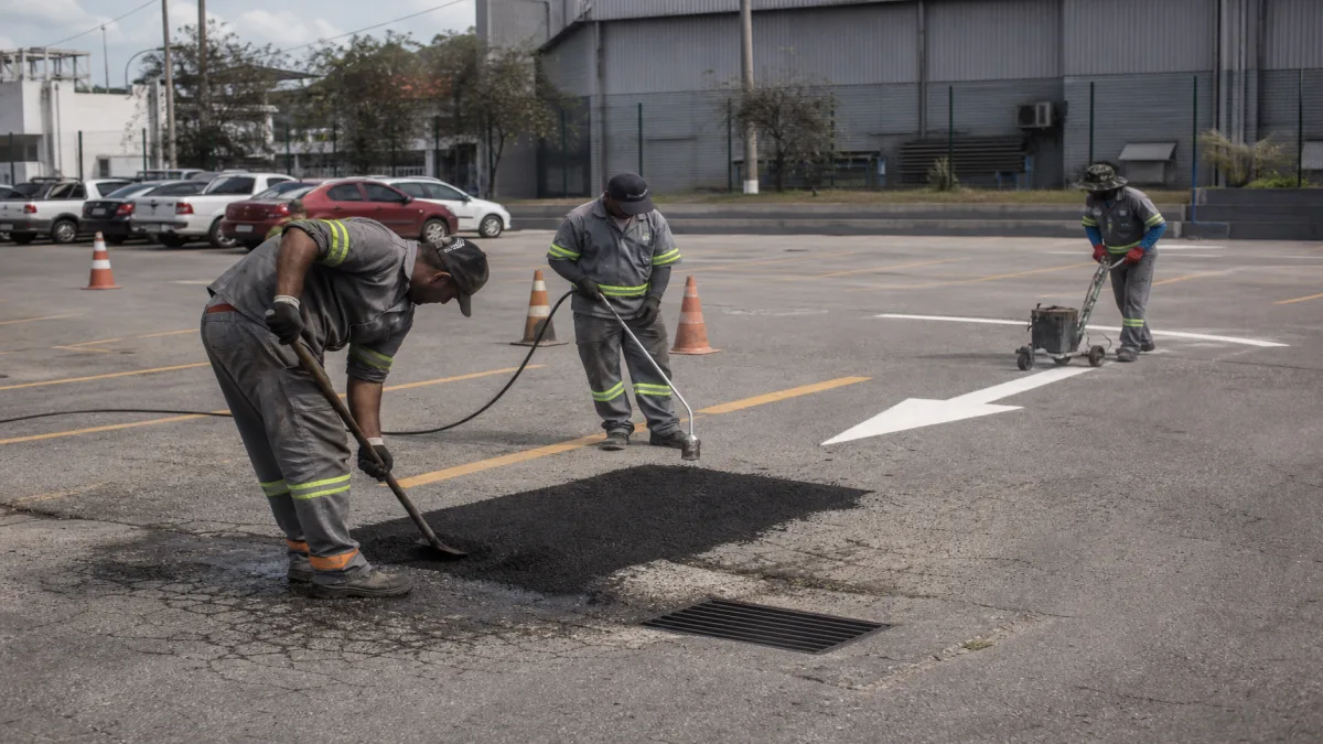 Equipe realiza manutenção de estacionamento com reparo asfáltico e repintura de vagas em área externa